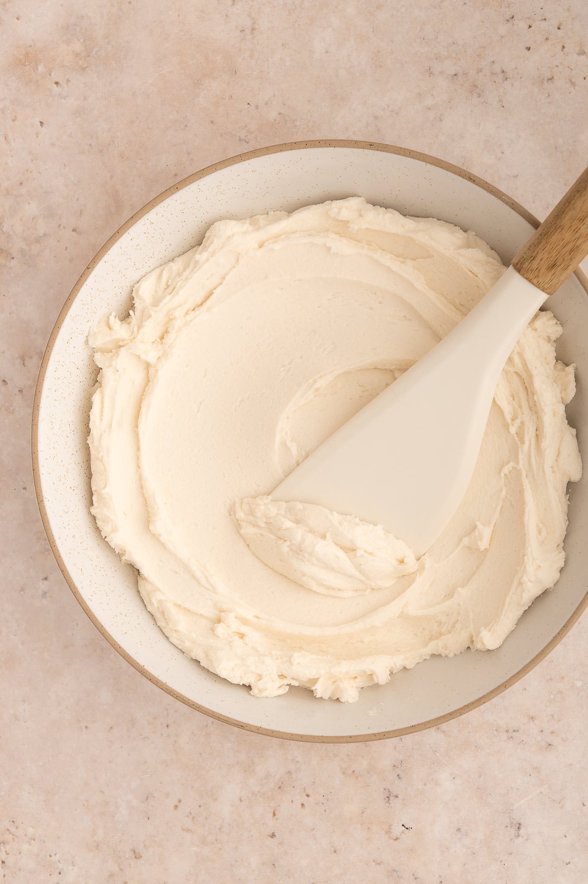 Creamy white frosting in a bowl with a spatula.