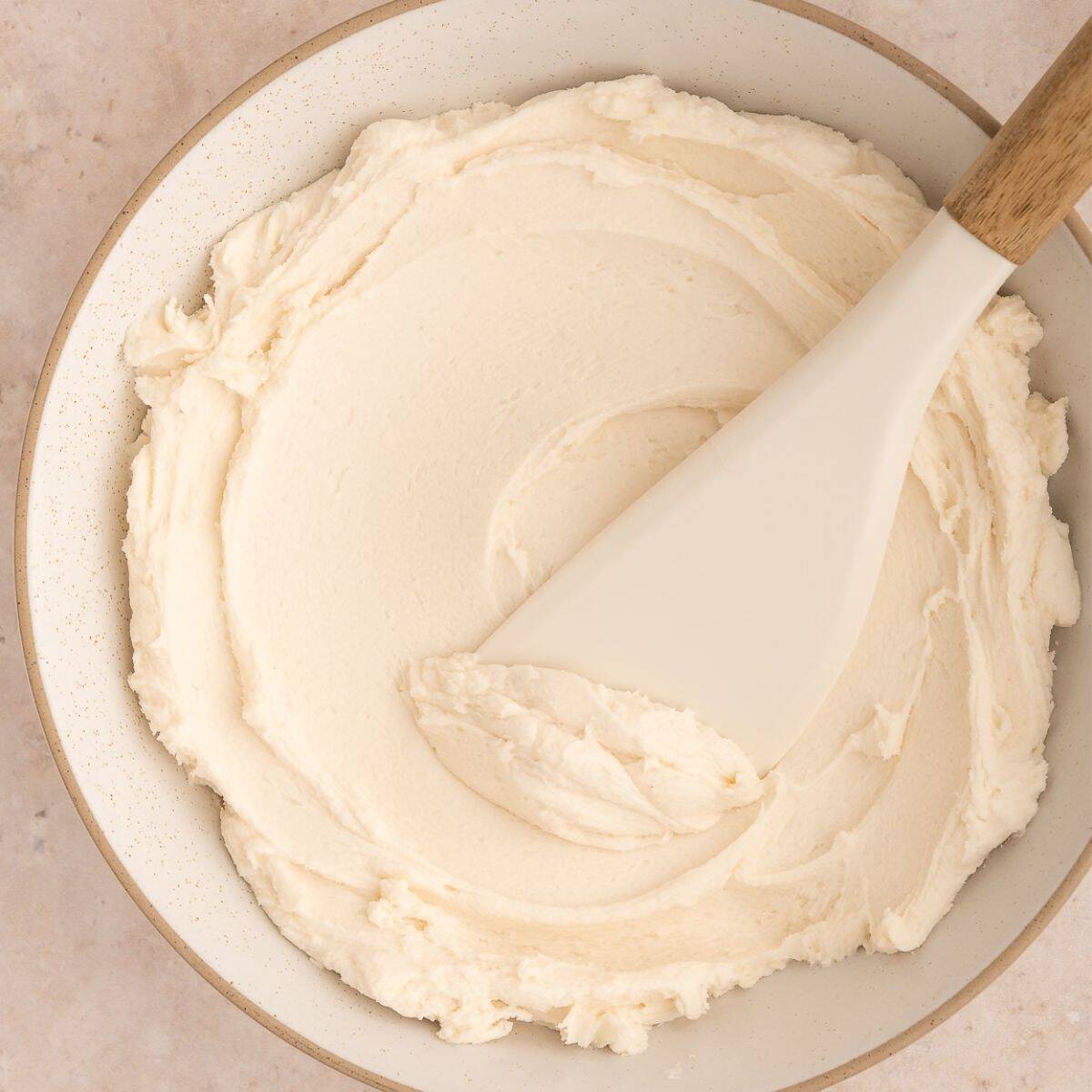 Creamy white frosting in a bowl with a spatula.